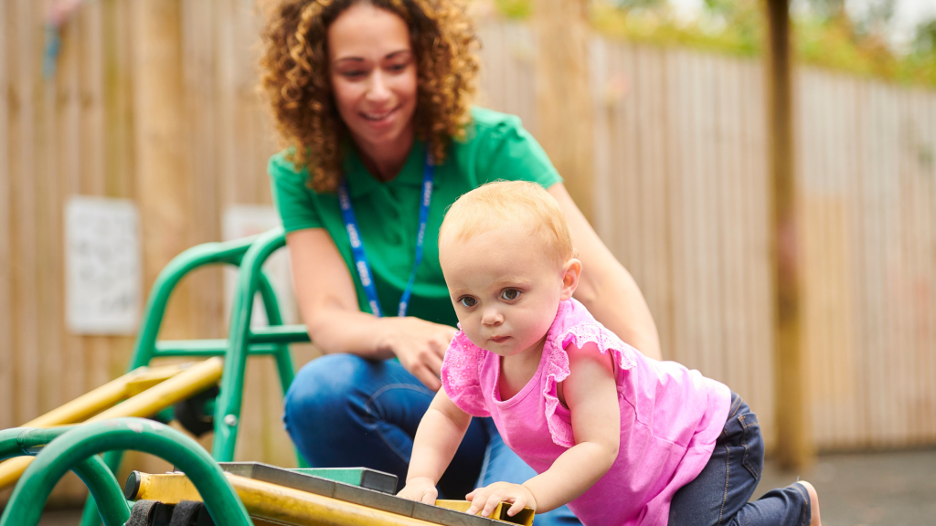 Baby on climbing frame being looked after by a female Kindergarten teacher